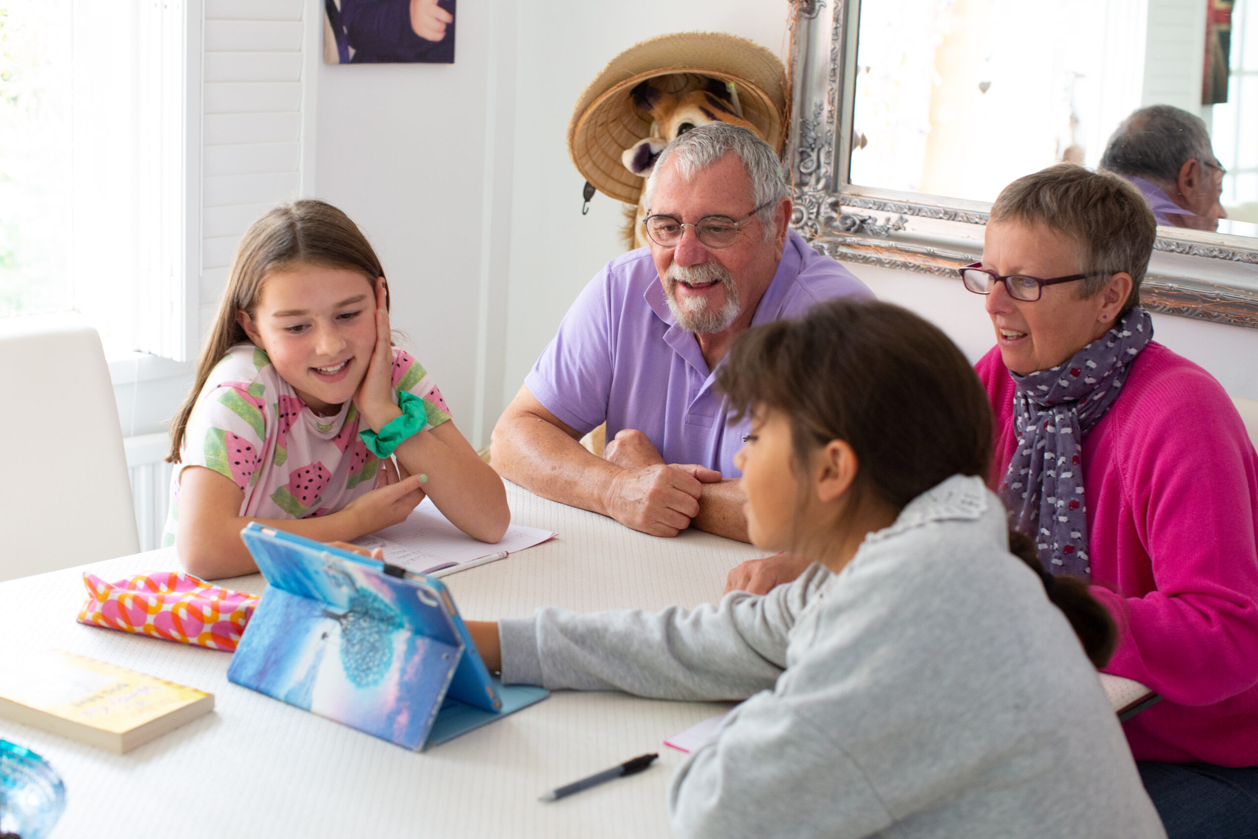 Older man and woman and two young children sitting by table looking at a tablet