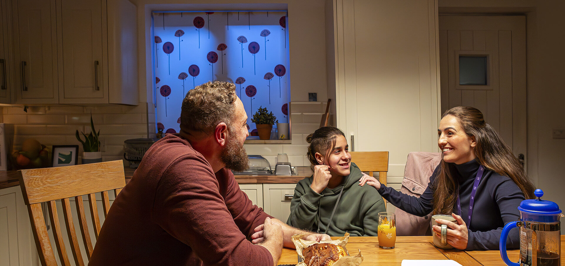 Social worker, teenage boy and male foster carer sitting by table chatting